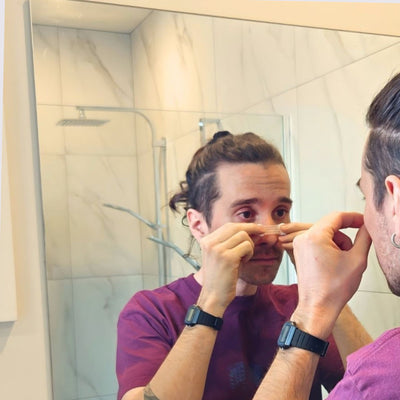 Person in a bathroom mirror placing a Hero2 nose strip